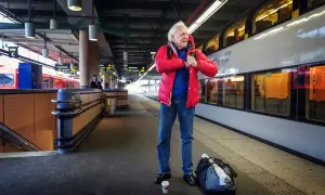 Äldre man i röd jacka på tågstationen, kanske på väg att resa som Kay Pollack.