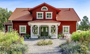 Vackert rött hus med vita detaljer, en veranda och en blomstrande trädgård. Ett perfekt exempel på att **bygga hus i gammal stil**.