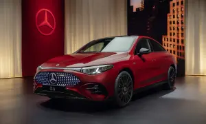 Elegancki, czerwony nowy Mercedes CLA z podświetlanym grillem i czarnymi felgami stoi na ciemnym tle z miejskim krajobrazem w tle.