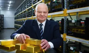 Mężczyzna w garniturze w magazynie Narodowego Banku Polskiego pokazuje sztabki złota, sugerując, ile złota ma Polska.