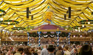 Festa della birra a Monaco: un'enorme folla festeggia sotto un tendone decorato con festoni gialli e neri, dominato da un gigantesco boccale di birra.