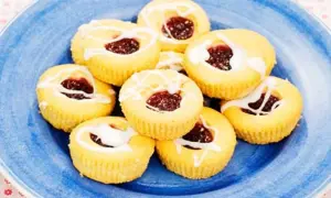 Hallongrottor recept: små, runda kakor med hallonsylt i mitten och glasyr på en blå tallrik.