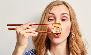 Kobieta z pałeczkami trzyma sushi przed ustami, zastanawiając się, czy sushi jest kaloryczne.
