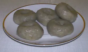Pięć okrągłych, szarych klusek śląskich z charakterystycznym wgłębieniem na talerzyku.