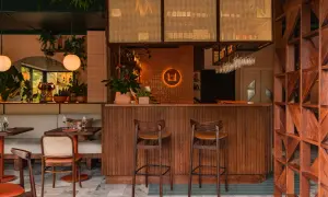 Przytulne bistro na piętrze z drewnianym barem, wygodnymi siedzeniami i mnóstwem zieleni.