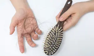 Une main tient une brosse à cheveux en bois, tandis que l'autre main montre une perte de cheveux. La lumière rouge met en évidence la perte de cheveux.