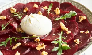 Rote Bete Carpaccio mit Burrata, Walnüssen und Rucola auf einem Teller.