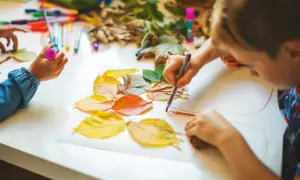 Niños creando arte con hojas de otoño. Actividades para trabajar las plantas en infantil, usando rotuladores y hojas secas para dibujar.