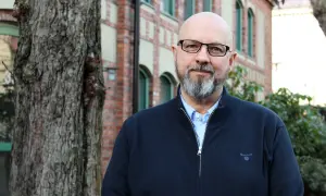 Kaj Stenman, en man med helskägg och glasögon, står framför en tegelbyggnad.