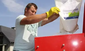Mężczyzna w żółtych rękawicach wsypuje zawartość worka z napisem Basamid do czerwonego urządzenia.