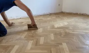 Trabajador aplicando barniz a un suelo de parquet en espiga. Consulta el precio lijado y barnizado parquet para renovar tu hogar.