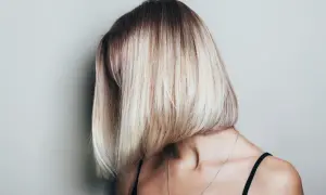 Kobieta z asymetryczną, blond fryzurą typu bob, z ciemniejszymi odrostami.