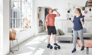 Un homme boit de l'eau pendant que sa compagne fait des exercices avec des haltères, développant ses muscles du bras.
