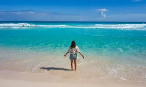 Frau steht im türkisfarbenen Meer, genießt das warme Wetter im Mexiko im Oktober. Der Strand ist sandig, das Wasser klar.