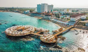 Idealne wakacje na Cyprze: turkusowe morze, plaża z leżakami i parasolami, hotel i restauracja na wodzie.