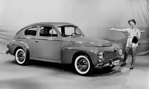 En glad kvinna poserar bredvid en klassisk Volvo PV 444.