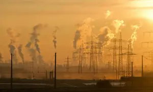 Dymiące kominy fabryk i linie energetyczne na tle zachodzącego słońca. Czy klimat się ociepla?
