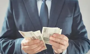 Mężczyzna w garniturze liczy polskie banknoty 100 zł. To zabezpieczenie należytego wykonania umowy.