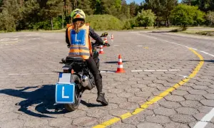 Osoba na motocyklu z tablicą "L" i kamizelką odblaskową na placu manewrowym.