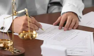 Prawnik podpisuje dokumenty, gdzie rozstrzygane jest prawo do zachowku a testament. Waga sprawiedliwości symbolizuje równowagę.