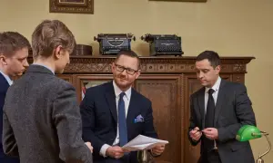 Czterech mężczyzn w garniturach w gabinecie, dyskutujących nad dokumentami.