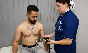 Pacjent z elektrodami EKG na klatce piersiowej, pielęgniarka podłącza urządzenie. To badanie, które odpowiada na pytanie: holter co to jest.