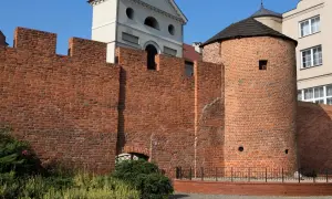 Kamienna baszta obronna, znana jako baszta Dorotka, z charakterystycznym stożkowym dachem, otoczona ceglanym murem.