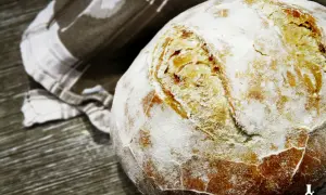 Świeżo upieczony bochenek chleba na drożdżach, oprószony mąką, leży obok lnianej ściereczki. Idealny przepis na chleb na drożdżach.