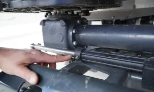 Dłoń wskazuje na element układu kierowniczego, prawdopodobnie kalamitkę, w silniku łodzi.