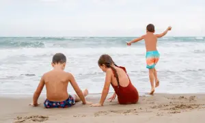 Dzieci bawią się na plaży, szukając **jastarnia atrakcje dla dzieci**. Chłopiec biega w stronę morza, dziewczynka i drugi chłopiec siedzą na piasku.