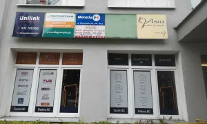 Szyldy firm ubezpieczeniowych i salonu fryzjerskiego na szarej ścianie budynku.
