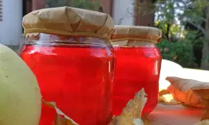 Due barattoli di gelatina di mele cotogne, con mele e foglie autunnali.