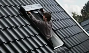 Un couvreur installe un volet roulant sur un toit en tuiles noires, un modèle velux 3uc b01 eu.