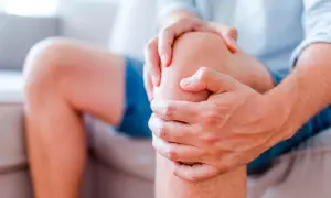 Mann hält sein Knie, das einen stechenden Schmerz im Knie anzeigt.