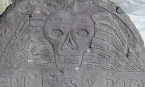 Kamienna płyta nagrobna z symbolem czaszki i skrzydeł, typowym dla purytanizmu, z fragmentem inskrypcji.