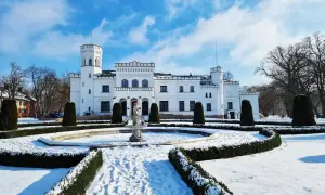 Biały pałac w Wielkopolsce, otoczony śniegiem i zimową aurą, z fontanną i zadbanym ogrodem.