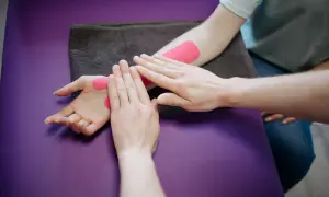 Fizjoterapeuta aplikuje taśmy kinezjotaping na nadgarstek pacjenta. Długość rehabilitacji po złamaniu nadgarstka zależy od wielu czynników.