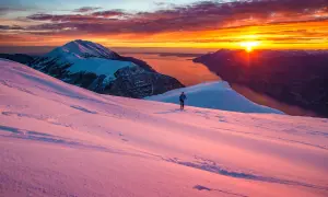 Alba infuocata sul lago di Garda in inverno. Un escursionista solitario cammina su un pendio innevato, godendosi la vista mozzafiato.