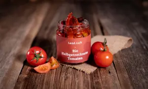 Glas mit halbgetrockneten Tomaten, frische Tomaten und Scheiben auf Holzhintergrund.