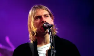 Kurt Cobain śpiewa do mikrofonu na tle fioletowej sceny.
