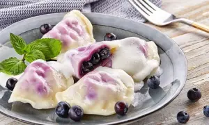 Pyszne pierogi z jagodami, polane śmietaną, ozdobione miętą i świeżymi owocami. Idealne na deser!