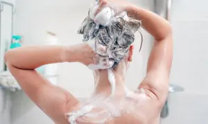 Persona lavándose el cabello con champú sin sulfatos, creando espuma abundante para una limpieza suave.