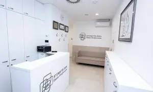 Nowoczesne wnętrze recepcji stomatologicznej z białym lady, kanapą i logo kliniki.