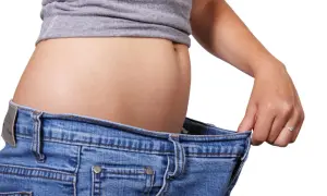 En kvinna håller upp sina jeans som är för stora, ett tecken på att hon lyckats gå ner i vikt efter graviditet.