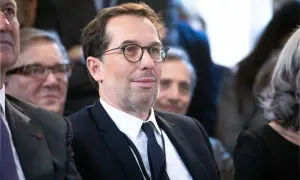 Un homme avec des lunettes, en costume noir, souriant.