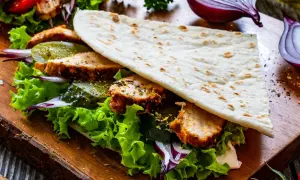 Pyszny placek pszenny piadina z kurczakiem, sałatą, ogórkiem i czerwoną cebulą na drewnianej desce.