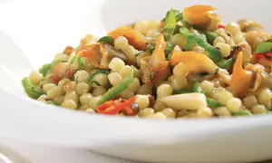 Un piatto di fregola sarda con vongole, peperoncino e zucchine, un sapore di mare e terra.