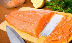 Un beau filet de truite saumonée prêt à être transformé en gravlax, avec du citron, de l'aneth et de l'ail en arrière-plan.