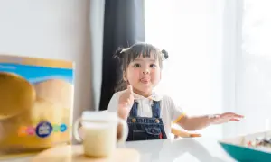 Mała dziewczynka z językiem na wierzchu, obok pudełka z mlekiem modyfikowanym, które zawiera kwasy omega dla niemowląt.