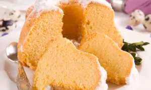 Puszysta babka z mascarpone, oprószona cukrem pudrem, z kilkoma kawałkami na talerzu. Obok leży łyżeczka.